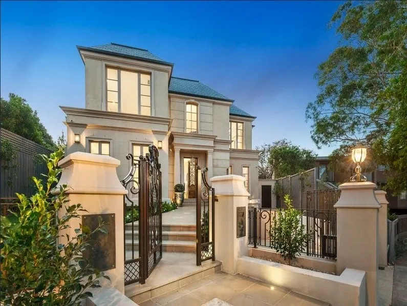 Angled twilight front façade of the completed Kew residence with wrought-iron entrance gates