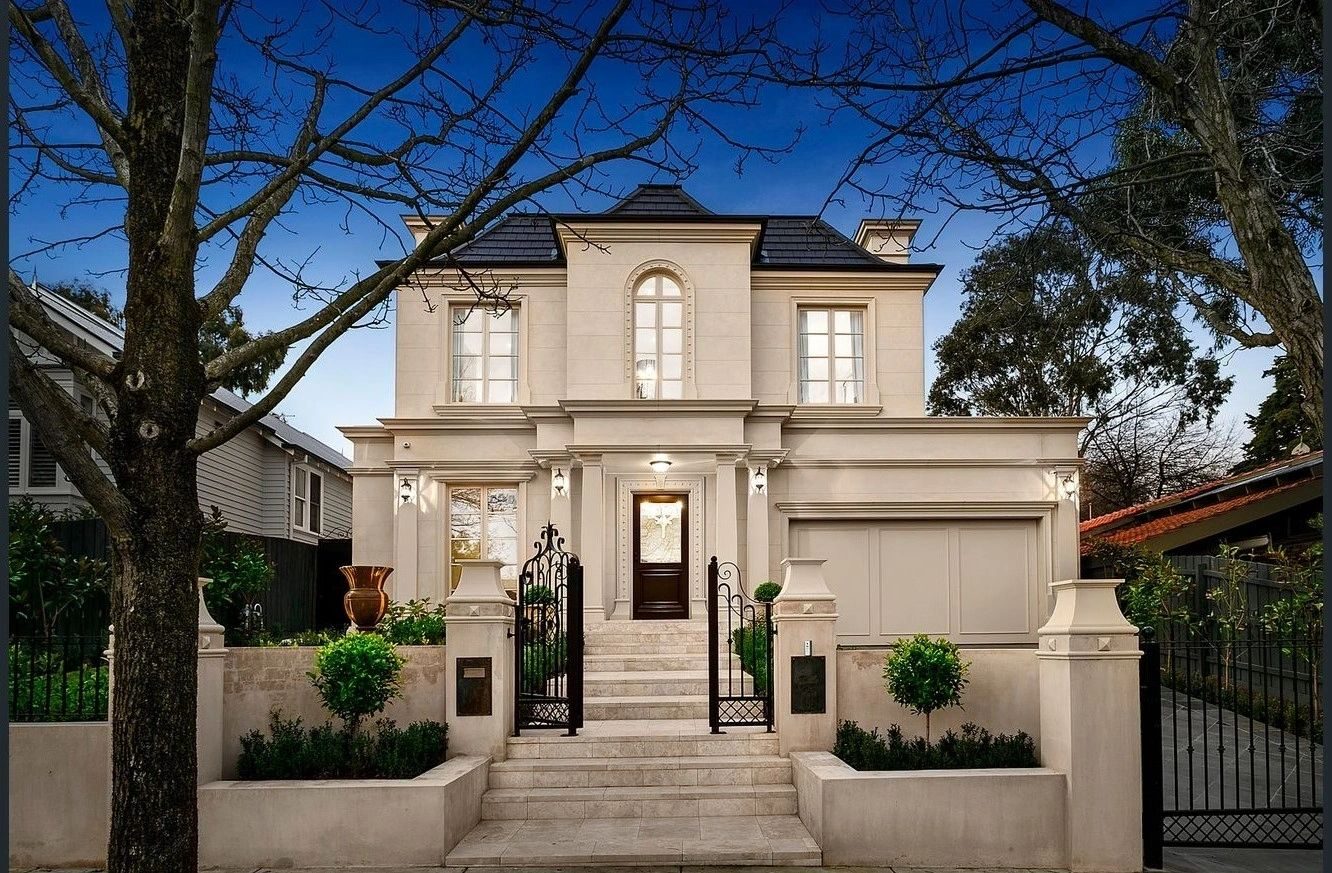Symmetrical rendered two-storey residence at twilight, framed by two mature deciduous trees